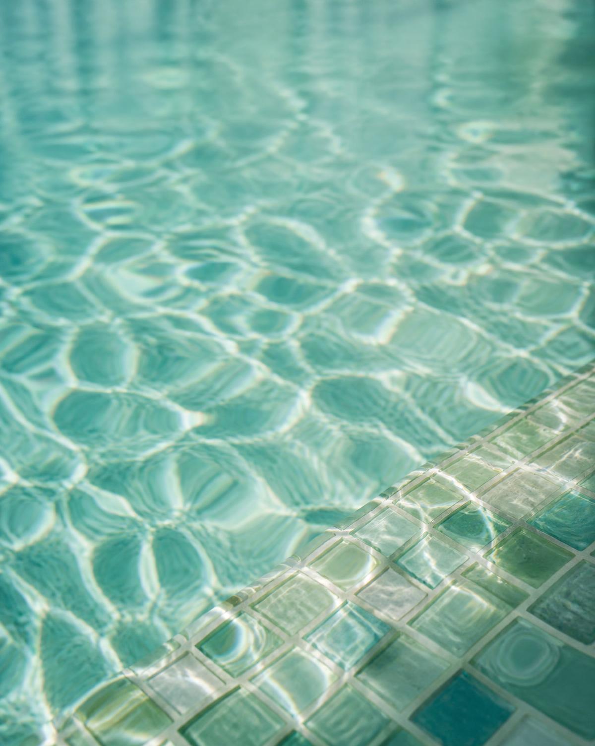 Sunlight across clear turquoise pool water beside glass mosaic tile